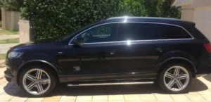 A side profile view of a black Audi Q7 luxury SUV parked on a tiled driveway.